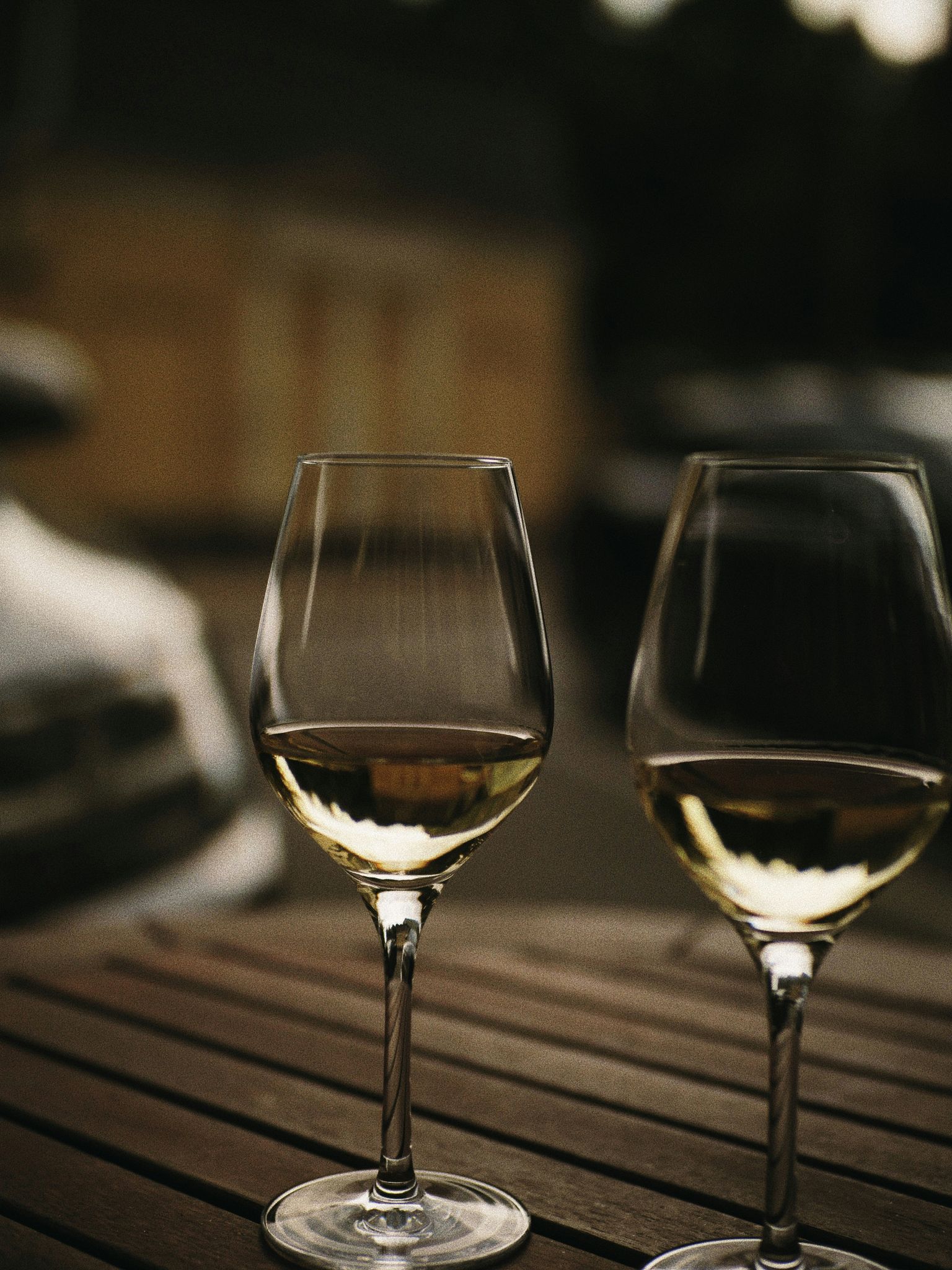 Zwei Weingläser mit goldgelbem Wein auf rustikalem Tisch.