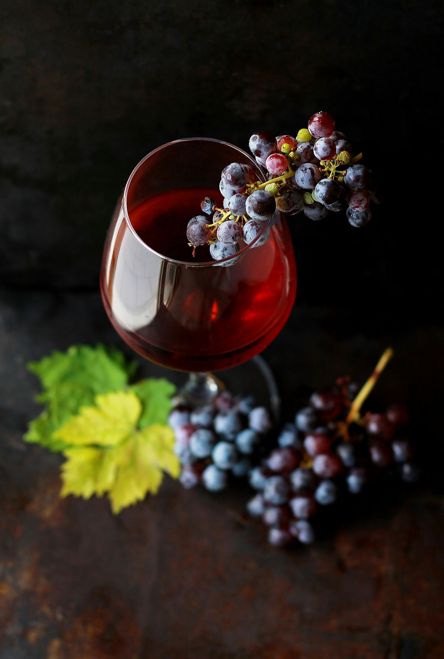 Gläsern mit Rotwein, umgeben von Weinblättern und Trauben auf dunklem Untergrund.