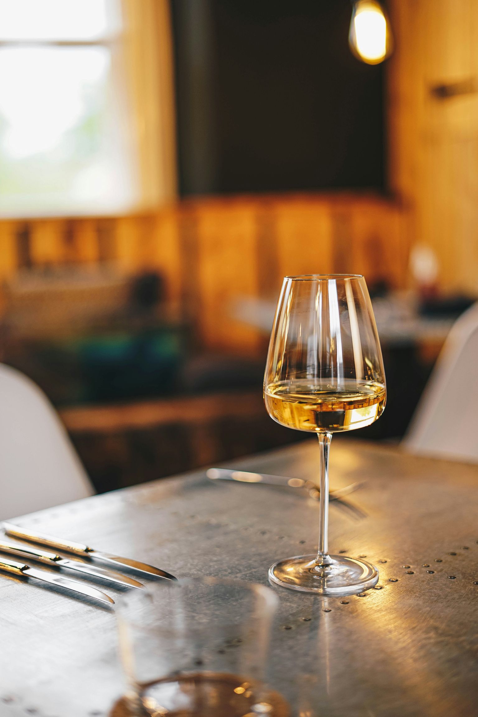 Ein Glas Weißwein auf rustikalem Tisch in gemütlichem Ambiente.